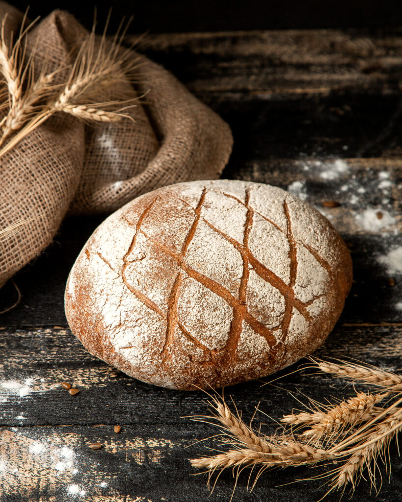 Artisan sourdough bread with flour-dusted crust and rustic scoring placed on wooden table with wheat grains