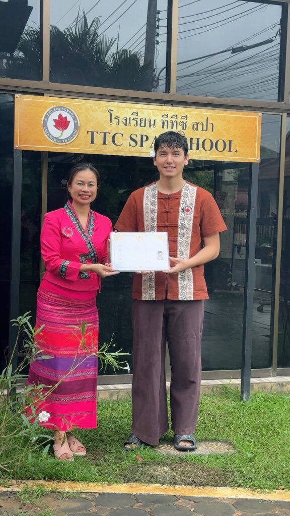Chef Altaycan from Dough Science project, holding his official Thai Massage Therapist certification next to his instructor in front of the TTC Spa School in Chiang Mai, Thailand.