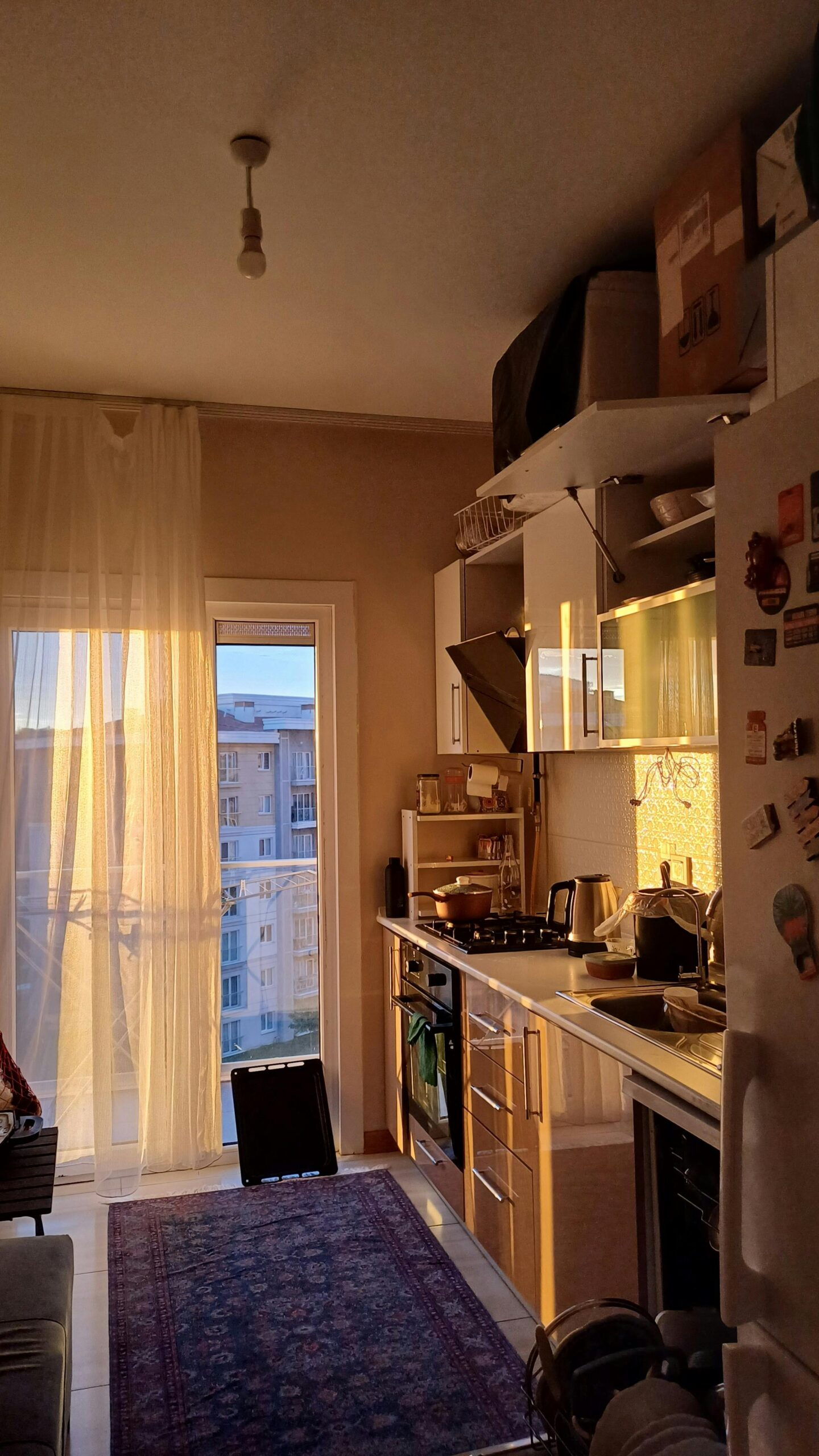 Warm sunset light illuminates a modern kitchen with a city view.