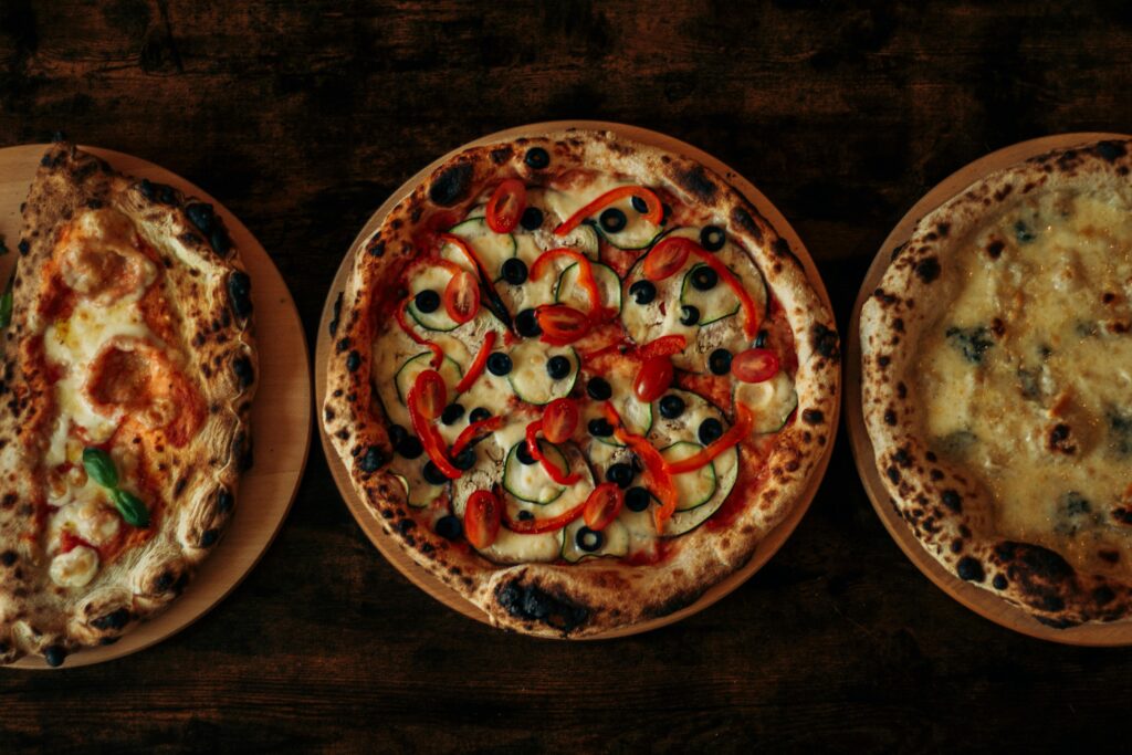 Three gourmet wood-fired pizzas with diverse toppings on a wooden table, showcasing Italian culinary craftsmanship.