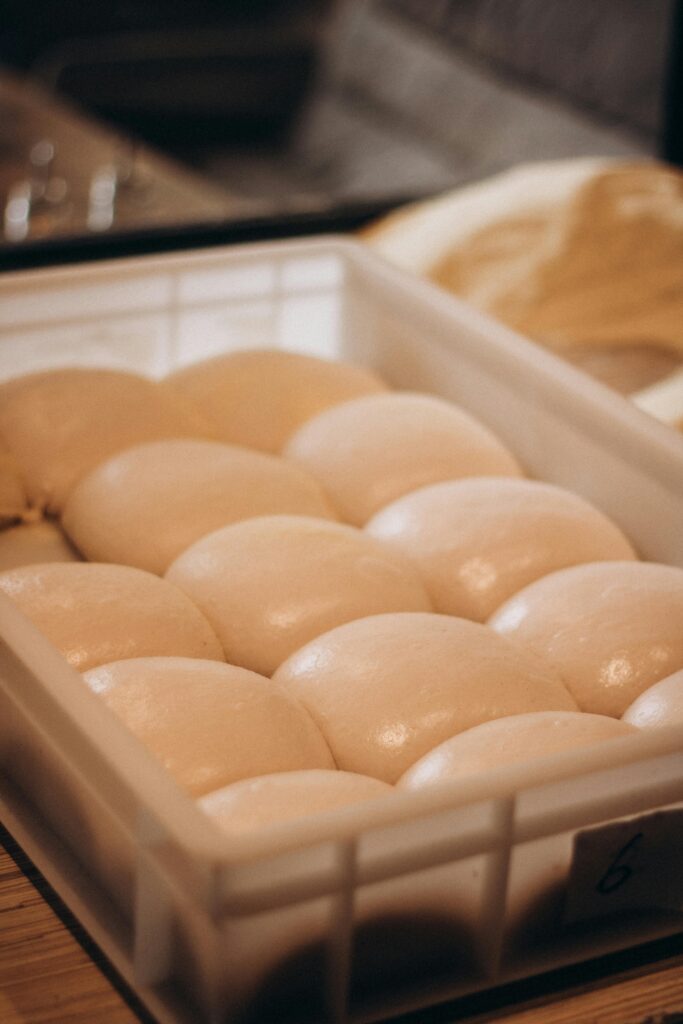 Close-up of smooth dough balls in a plastic tray, ideal for bread making or pizza preparation.