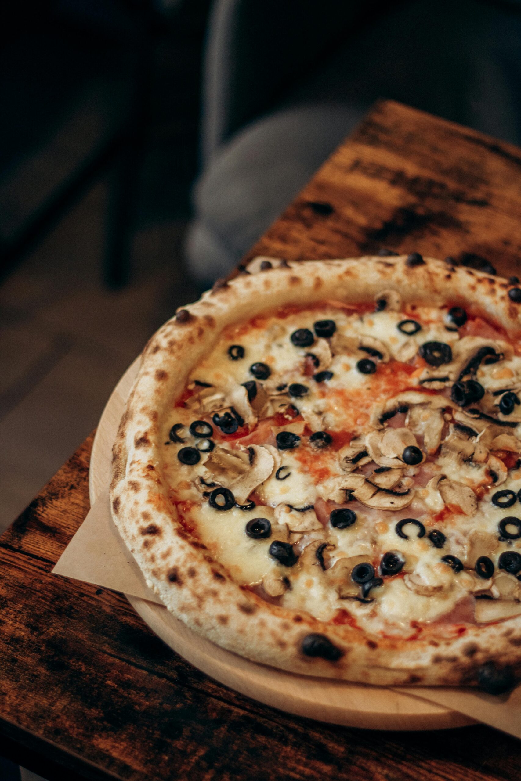 Savory mushroom and olive topped pizza on a rustic wooden table, perfect for a cozy meal.